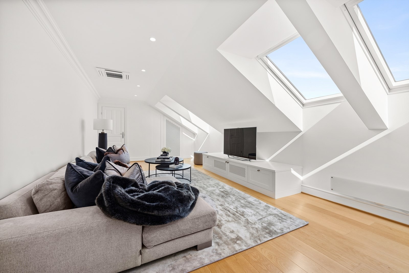 I denne etasjen ligger også husets fjerde stue. Rommet bader i naturlig dagslys takket være de store Velux-takvinduene, og overflatene har lyst parkett på gulvet, innfelte downlights og hvitmalte vegg- og takflater. Galleribilde