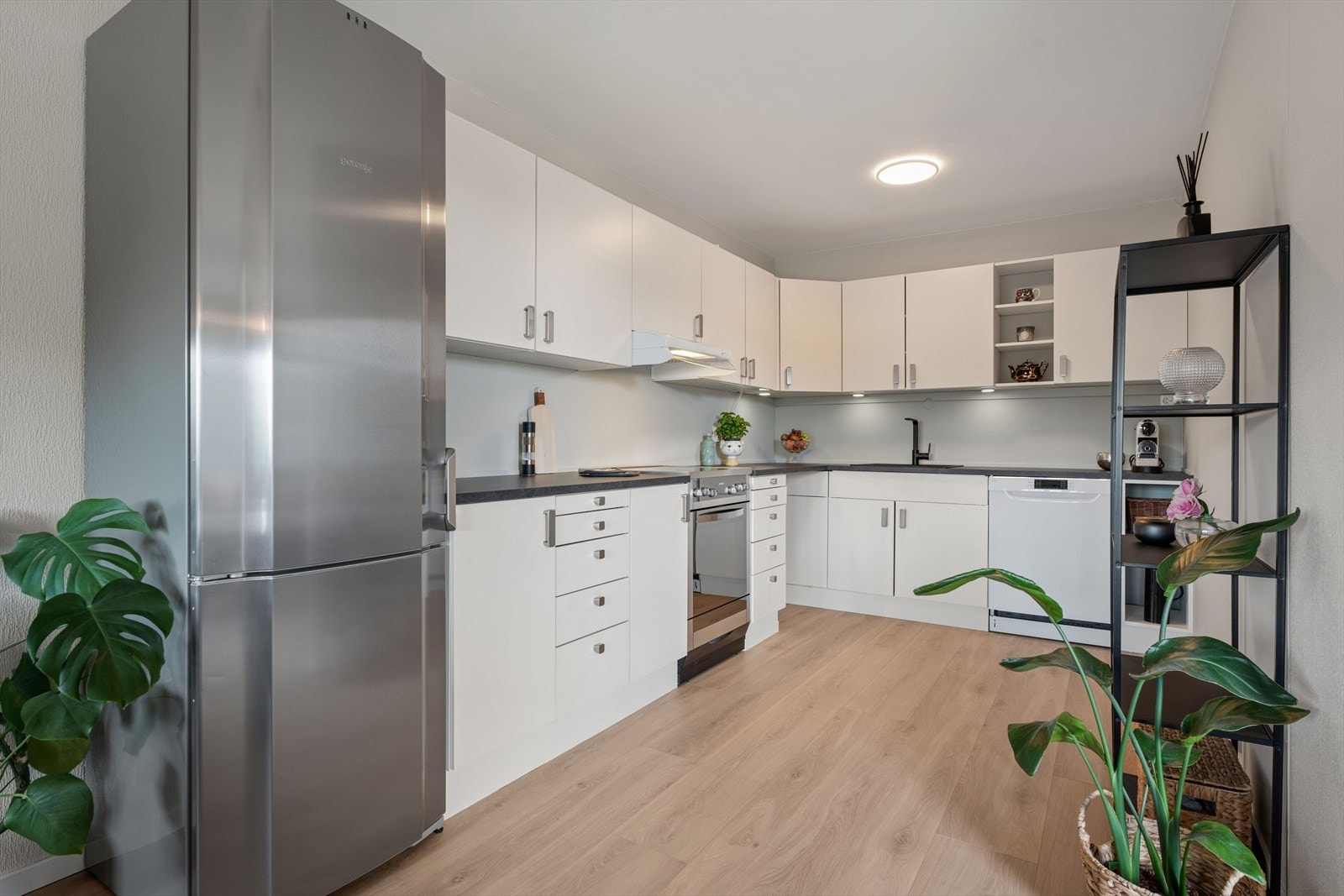 Kjøkkenet har en tidløs og funksjonell utforming med hvite, glatte fronter som gir et rent og moderne uttrykk. Benkeplatene er laminert og byr på gode arbeidsflater for matlaging og daglig bruk. Galleribilde