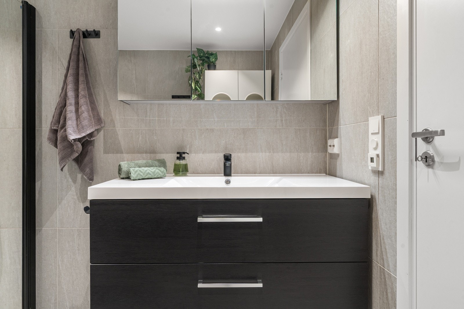 Badet er utstyrt med innredning med servant, dusjvegger av glass og dusjgarnityr på vegg, samt monterte downlights.
