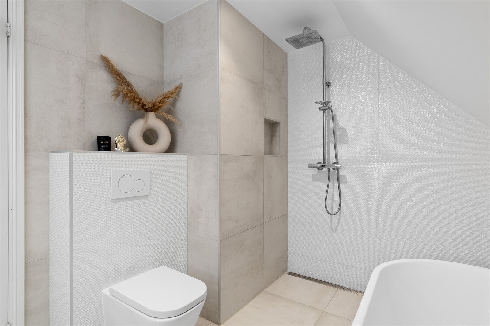 Badet er smakfullt innredet med vegghengt servantinnredning, høyskap, speil med integrert LED-belysning, et praktisk dusjhjørne, badekar og vegghengt toalett. Galleribilde