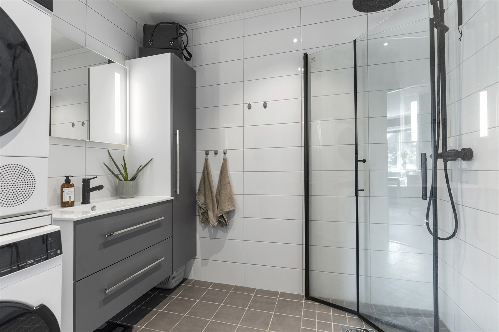 Delikat, flislagt bad med varme i gulv. Badet inneholder dusjhjørne, speil med belysning, heldekkende servant med skuffeseksjon, høyskap, toalett og opplegg for vaskemaskin/tørketrommel. Galleribilde