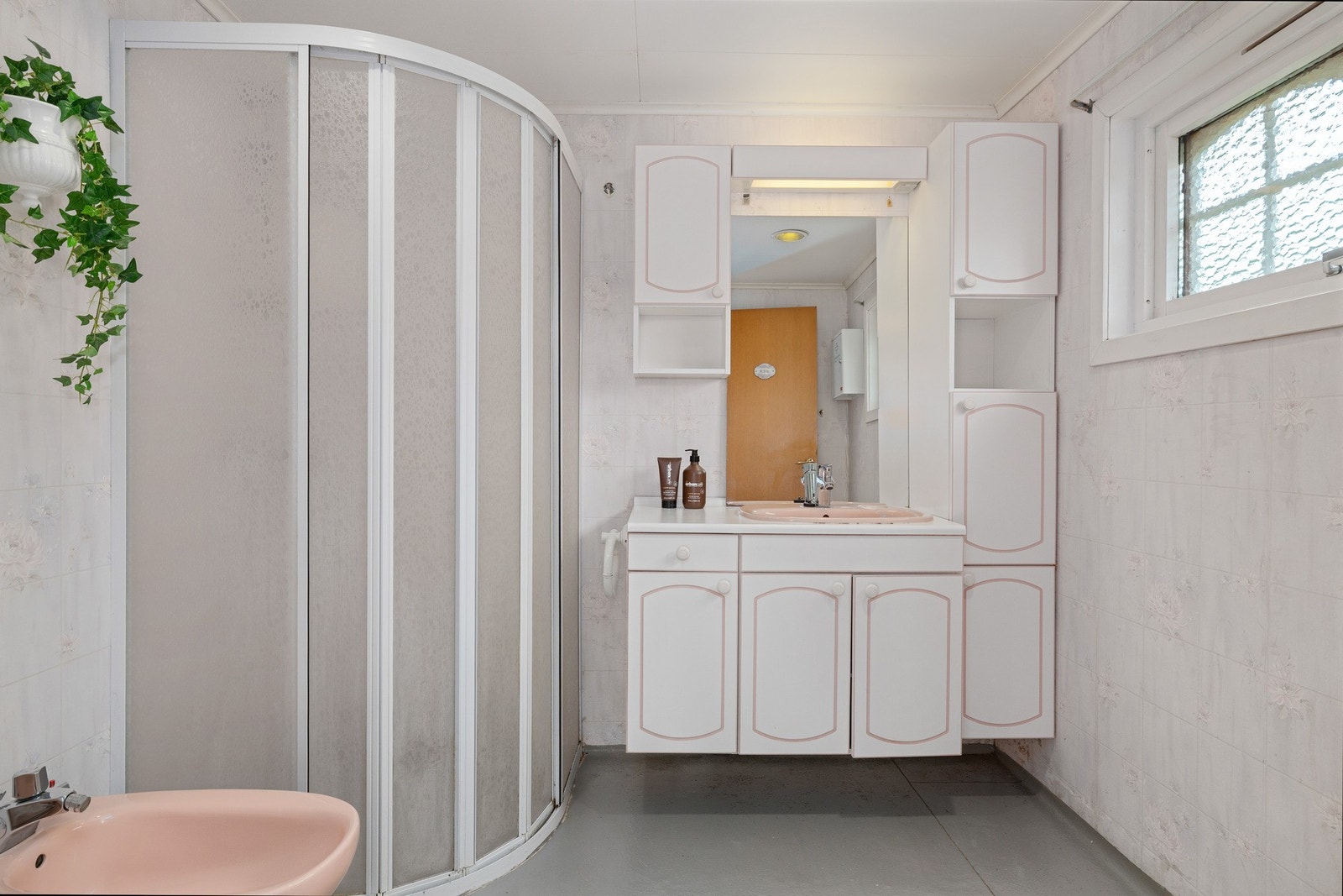 Badet har våtromstapet på vegger og vinylbelegg på gulv, rommet er innredet med en romslig servant, toalett og dusjvegger/ hjørne. Galleribilde