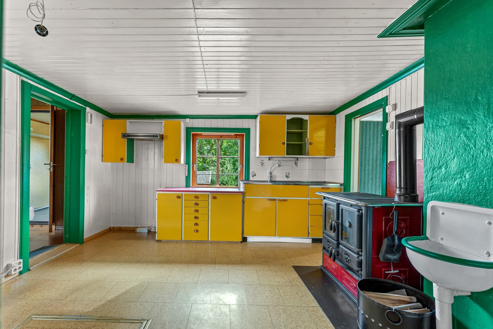 Kjøkkenet er romslig og har et karakteristisk uttrykk med gule fronter og markante grønne detaljer. Vedovnen er et naturlig blikkfang og tilfører både atmosfære og et nostalgisk preg til rommet. Galleribilde