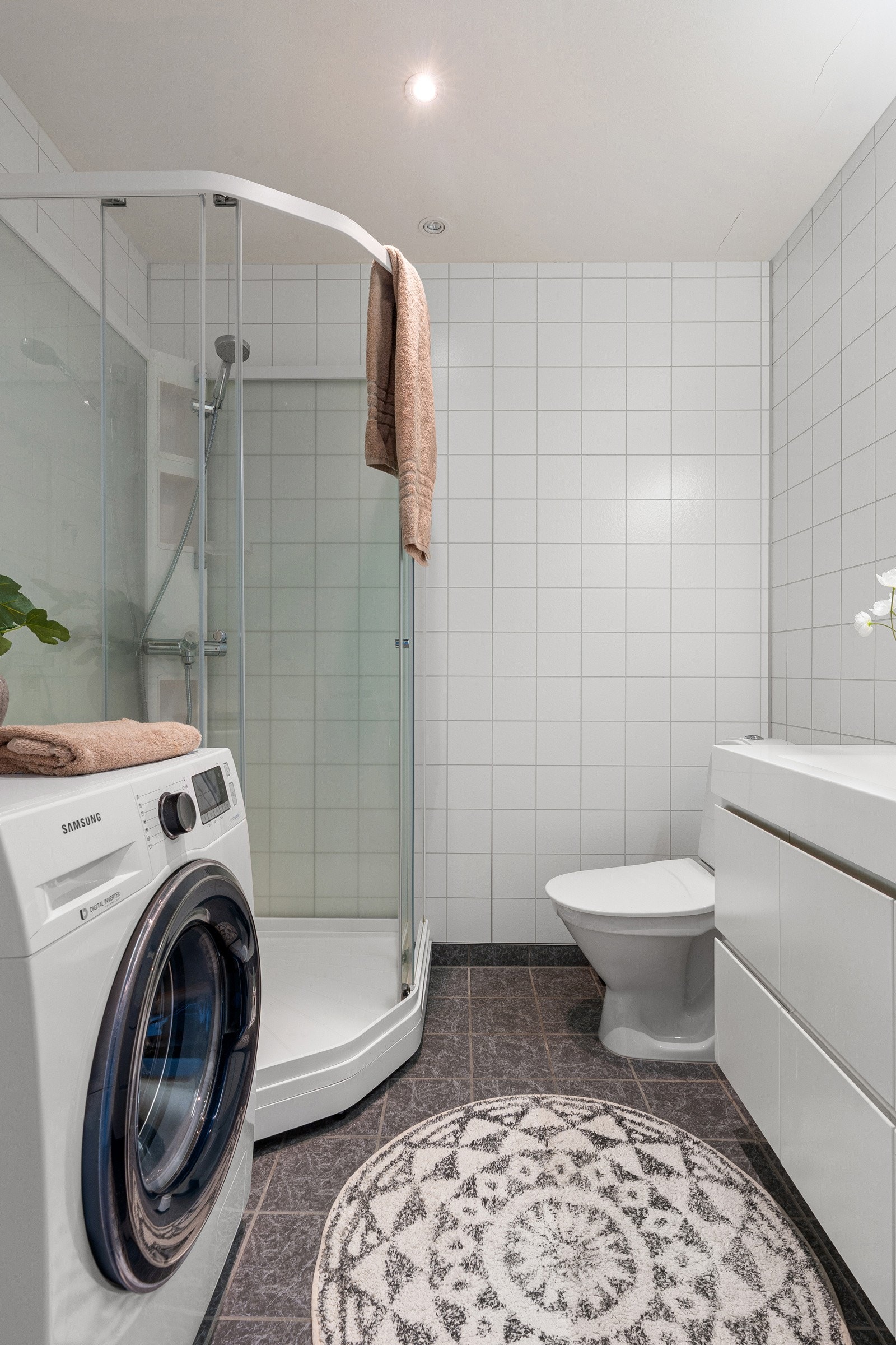 Moderne flislagt bad med opplegg for vaskemaskin, wc og dusjkabinett av nyere dato.