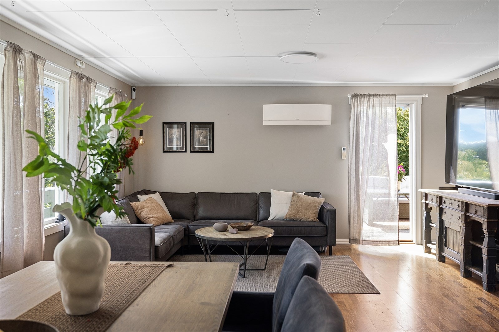 Stuen er lys og romslig, med store vindusflater mot de grønne omgivelsene og direkte utgang til verandaen. Varmepumpe fra Daikin. Galleribilde