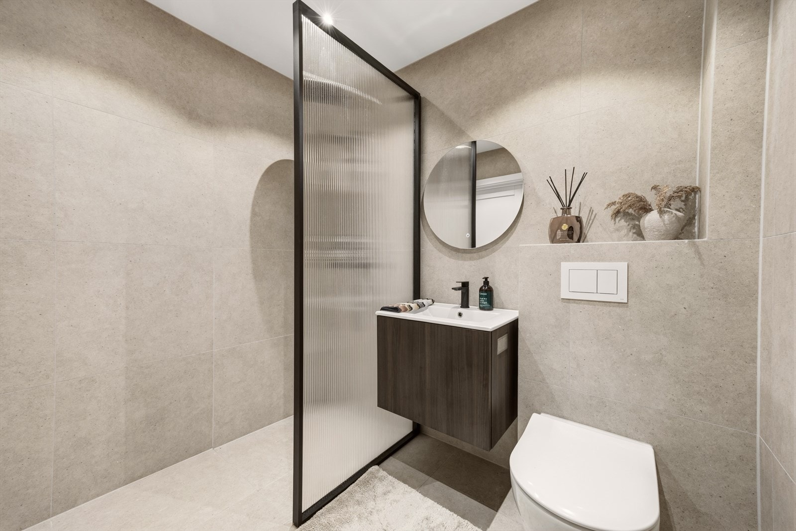 Badet er innredet med servant med underskap, speil med belysning, dusjnisje med glassvegg og veggmontert toalett Galleribilde