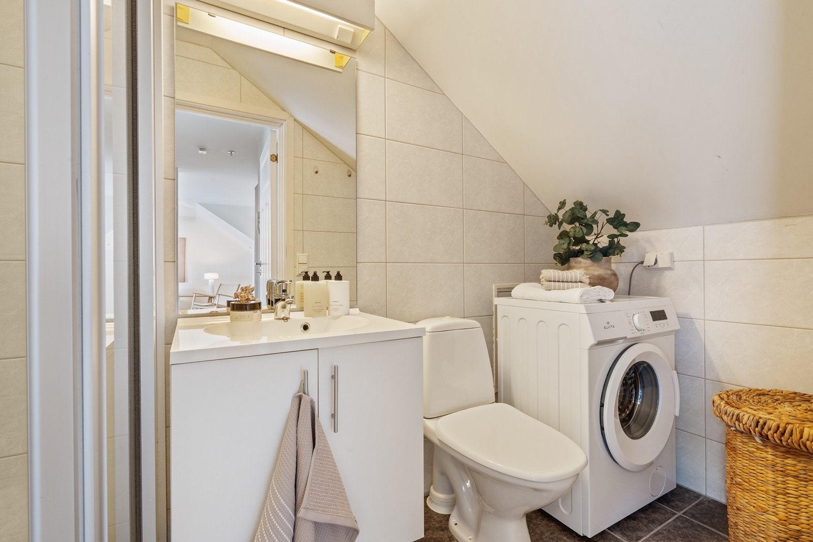 Badet er pent helfliset og inneholder servant i møblement, speil og belysning, dusjkabinett og gulvstående toalett. Galleribilde