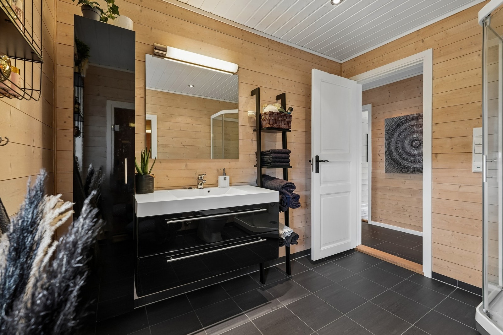 Badet er romslig og innredet med sort høyglans baderomsinnredning, dusjkabinett og gulvmontert toalett. Galleribilde