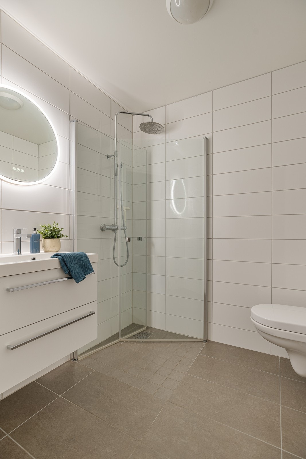 Lyst bad med vegghengt toalett, baderomsinnredning og dusjvegger/garnityr. Galleribilde