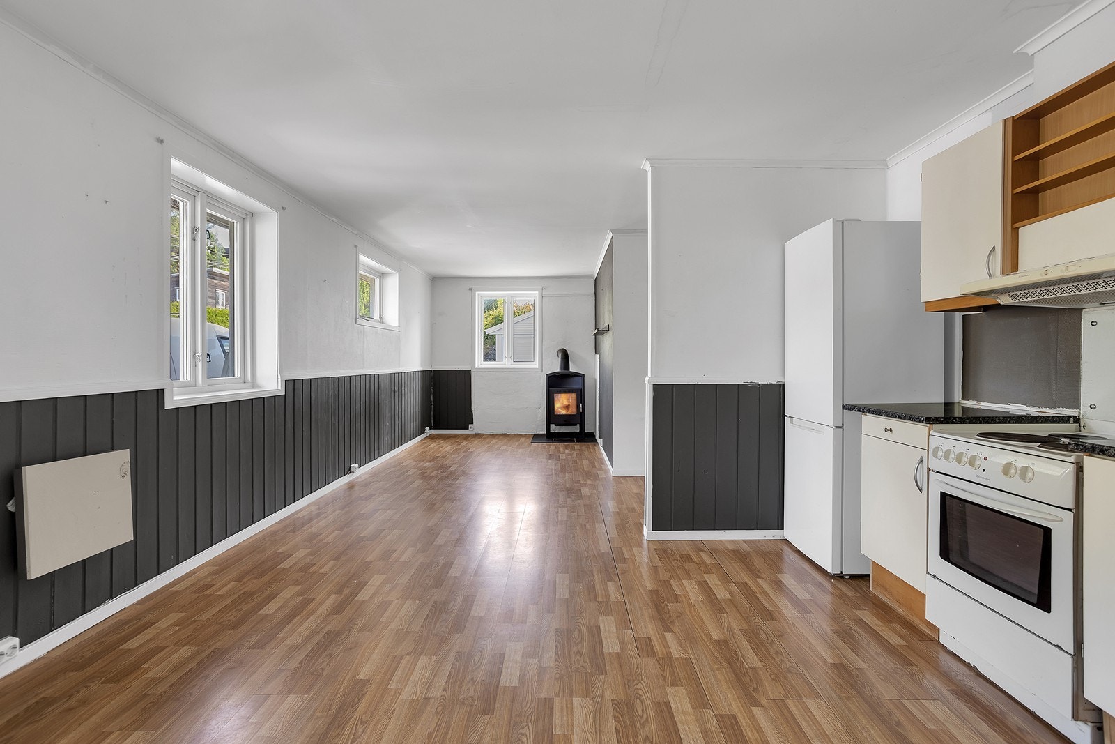 Stuen er langstrakt med flere vinduer som slipper inn dagslys, og en koselig vedovn i den ene enden av rommet. Galleribilde