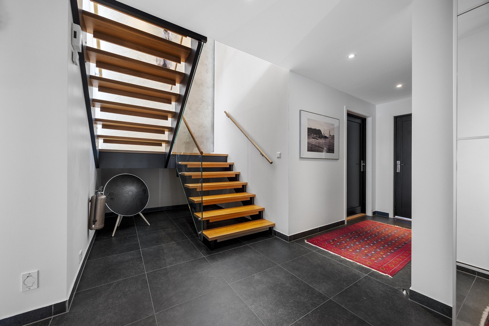 Trappen i tre og metall gir en moderne forbindelse mellom etasjene. Hall er med flislagt gulv med varmekabler. Downlights i tak. Galleribilde