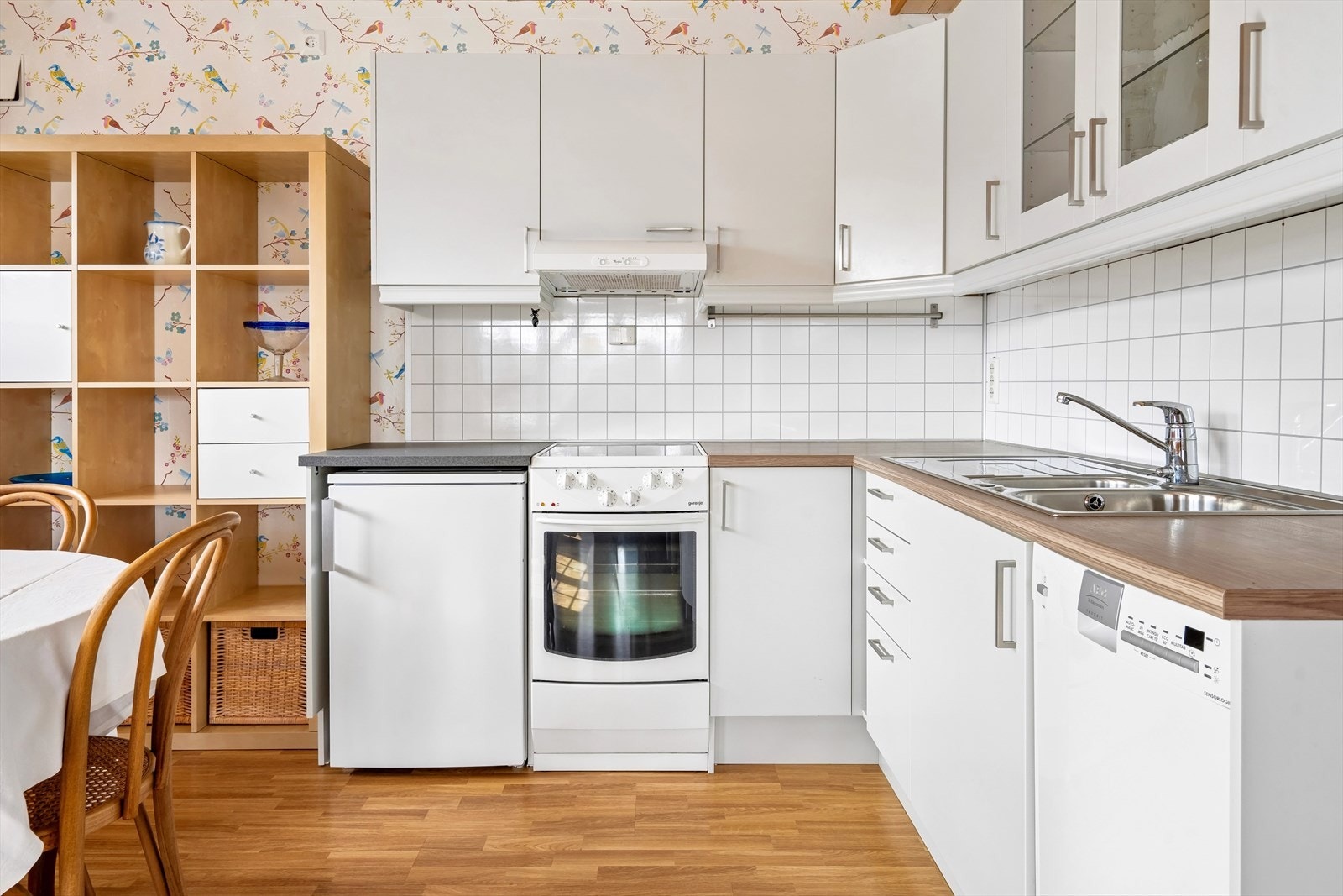 Kjøkkenet er innredet med slette, hvite fronter, frittstående hvitevarer, og oppvaskkum i stål. Galleribilde