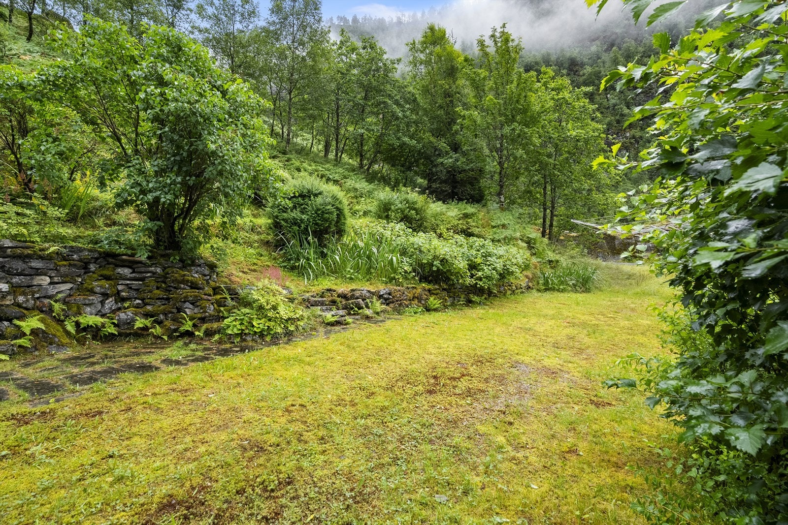 Uteområde med natursteinsmurar og grasbakkar, her har ein god plass til å opparbeide hage Galleribilde