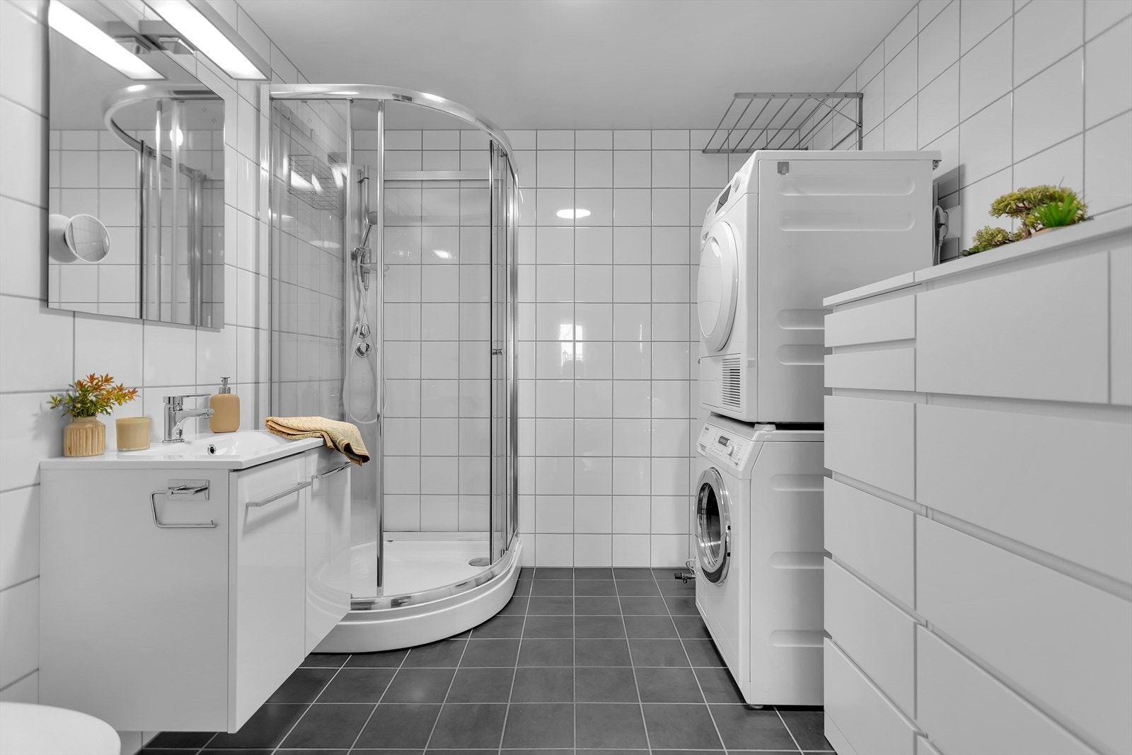 Pent og innbydende bad med flislagte overflater, dusj, servant, toalett og opplegg for vaskemaskin. Galleribilde