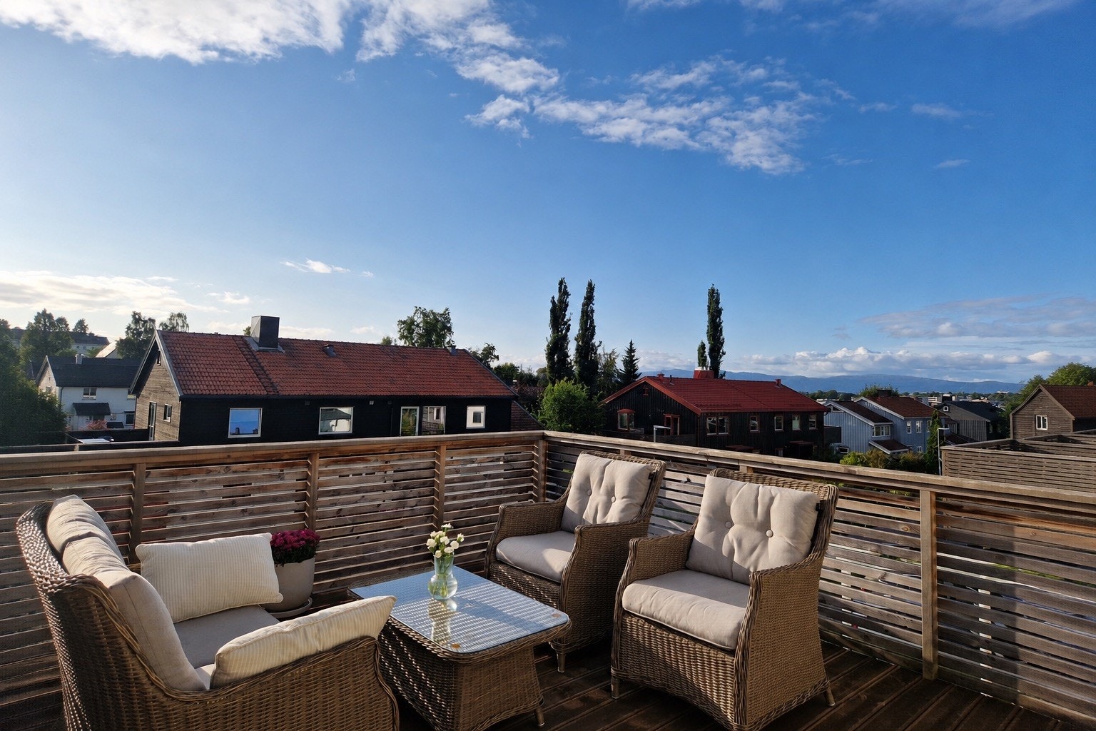 Fra takterrassen har du en flott utsikt over nabolaget med sine karakteristiske hus og røde tak, omkranset av frodig grønt og med fjell i horisonten. Her ligger forholdene godt til rette for å nyte slutten av kvelden i kveldssolen. Foto tatt av selger. Galleribilde