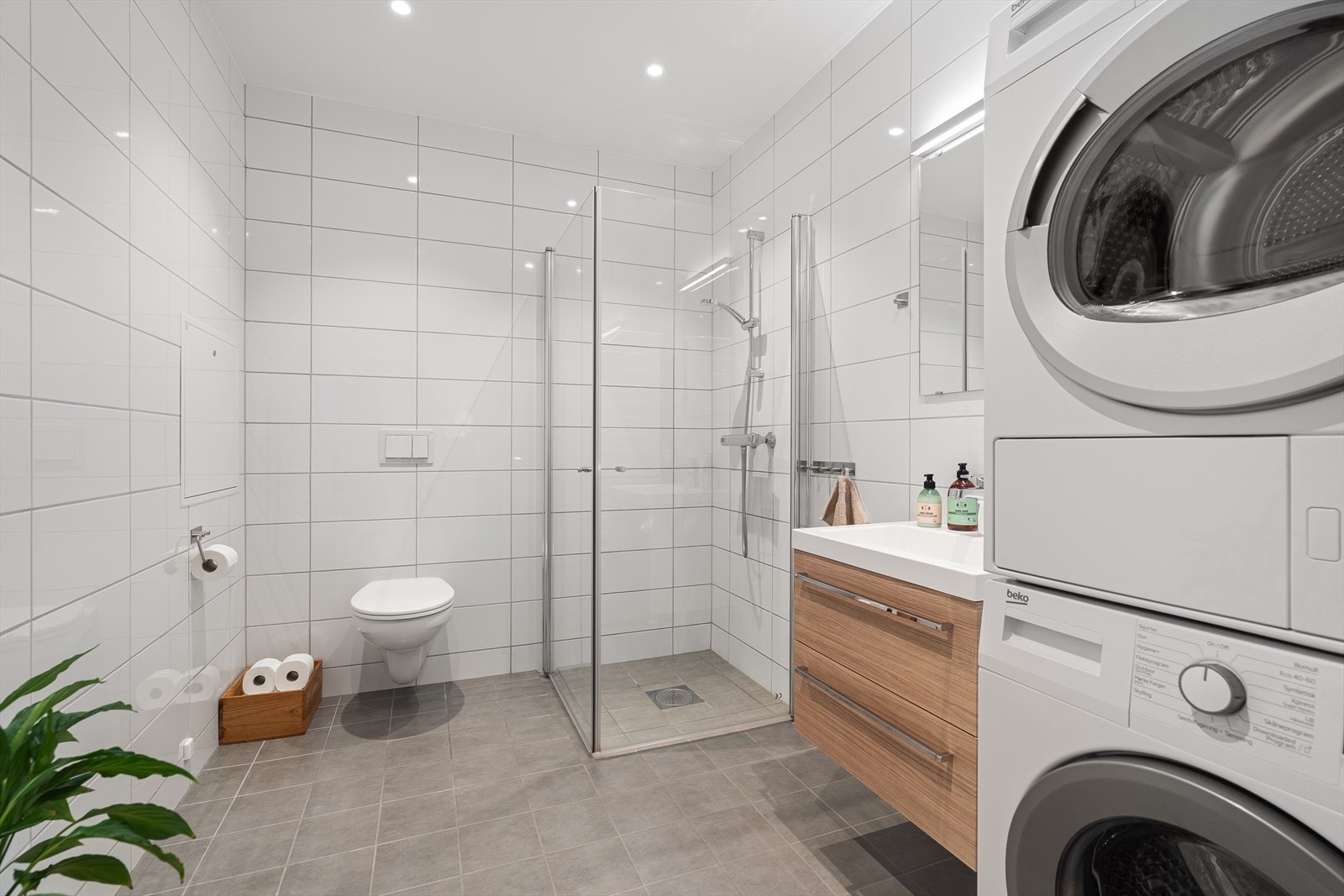 Videre inn finner du badet som er helfliset med varme i gulvet. Det inneholder en dusjnisje med innfellbare dusjdører, vegghengt toalett, samt plass og opplegg for vaskemaskin/tørketrommel. Galleribilde