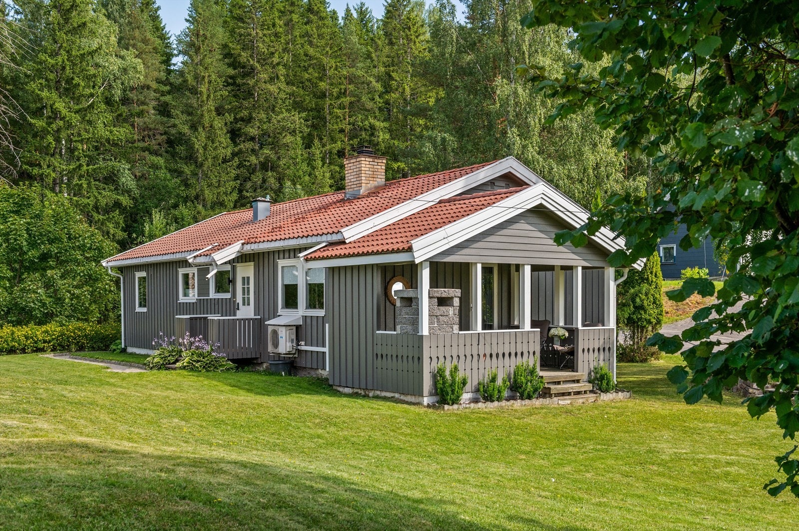 Koselig og landlig beliggende på et måls stor tomt med svakt skrånet terreng, pent opparbeidet med plen og beplantninger. Galleribilde