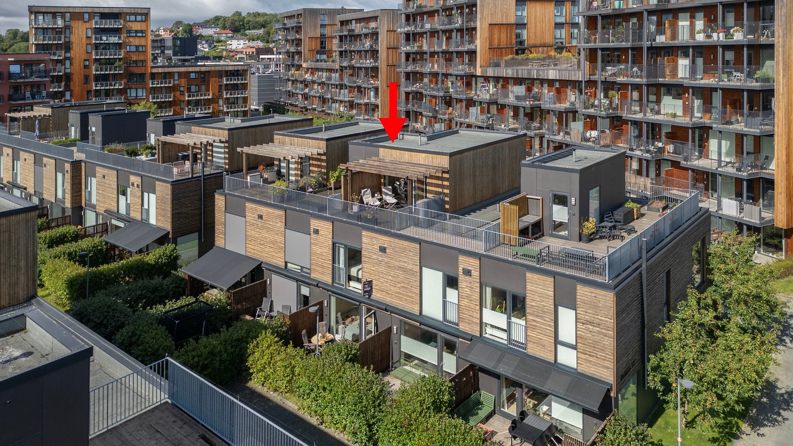 Dronefoto, rød pil markerer boligens gode plassering i feltet. Bildet viser også kombinasjonen av moderne bebyggelse og grønne omgivelser. Galleribilde