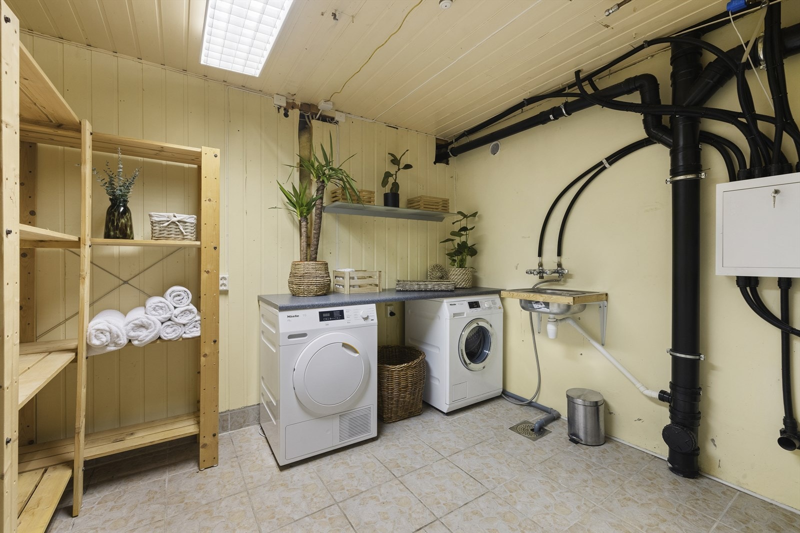 Underetasjen byr også på et romslig vaskerom med flislagt gulv, opplegg for vaskemaskin og tørketrommel under benk, stor utslagsvask og rikelig med hylleplass. Galleribilde
