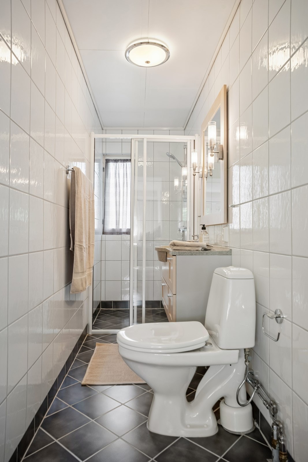Badet er innredet med servant, toalett og dusjhjørne. Vegger og gulv er flislagt, og gulvet har elektriske varmekabler. Galleribilde