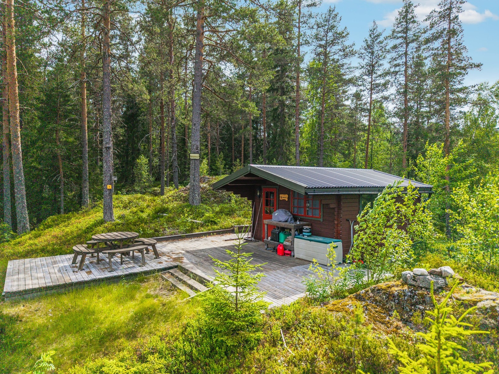 Hytte nr. 3 ligger høyt og tilbaketrukket på tunet, skjermet av furutrær og med en stor treplatting rundt hytta. Galleribilde