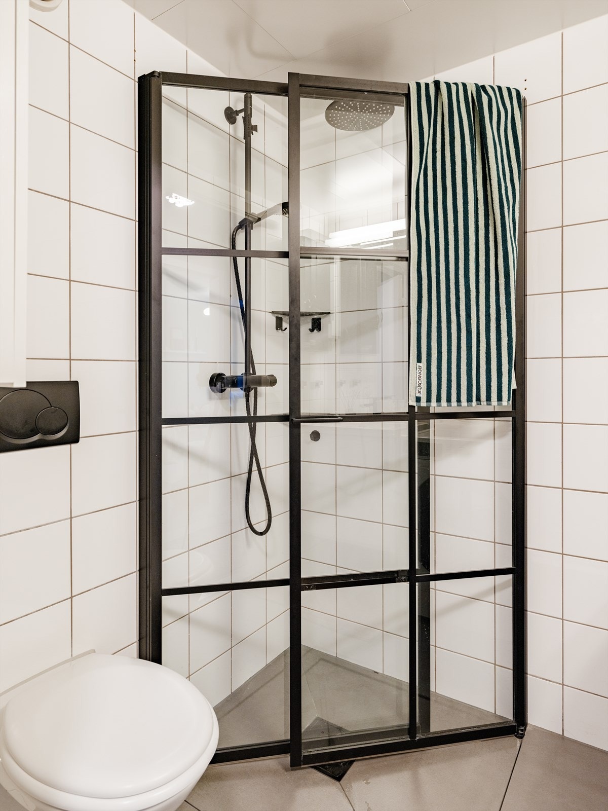 Badet er innredet med vegghengt toalett og en moderne baderomsinnredning. Dusjhjørne med innfellbare glassdører. Glassdørene har moderne, sorte profiler Galleribilde