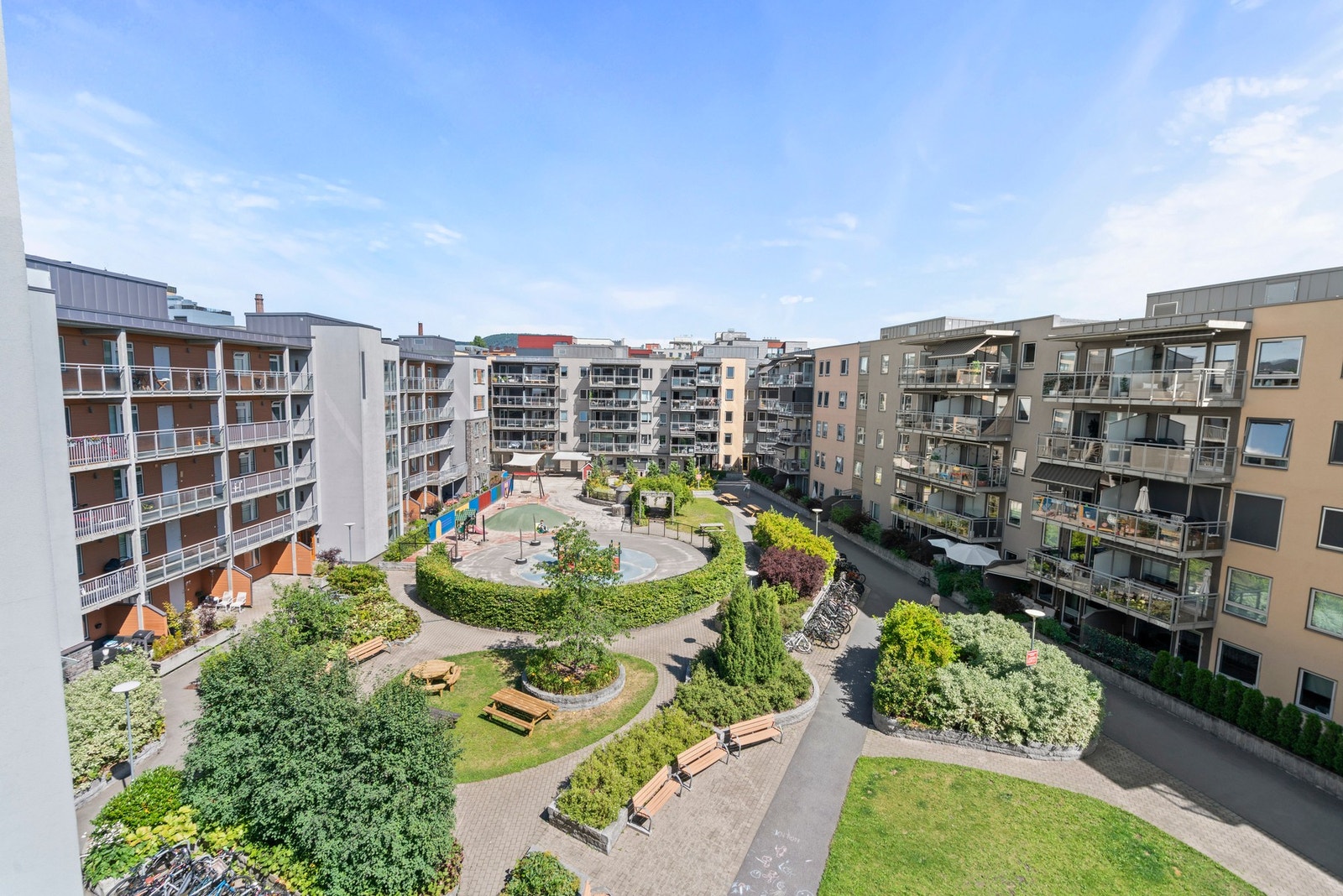 Stort og velholdt fellesområde med grønne plener, beplantning, sitteplasser og gangveier mellom bebyggelsen. Galleribilde