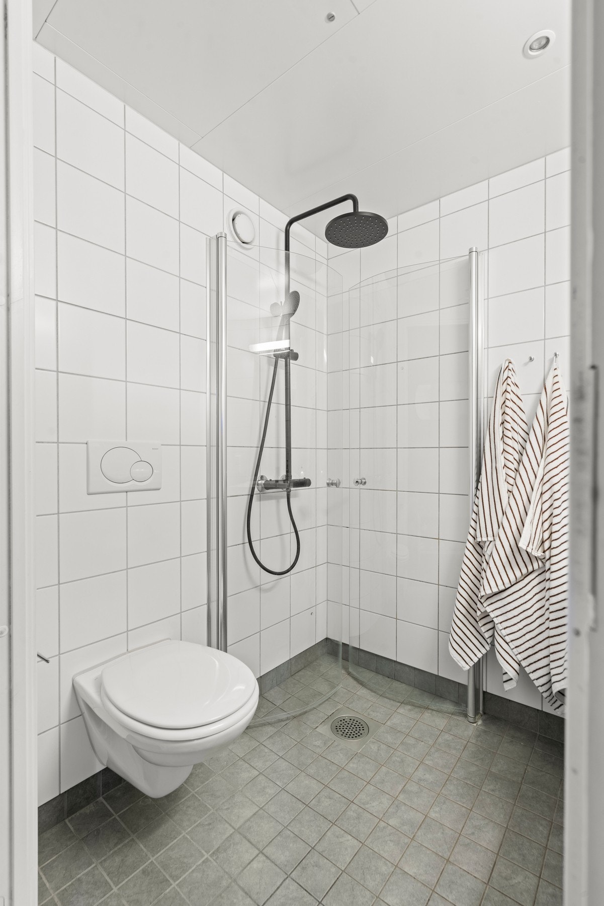 Badet er utformet som en prefabrikkert baderomskabin fra byggeåret, med flislagt gulv og vegger samt praktisk dusjløsning. Galleribilde