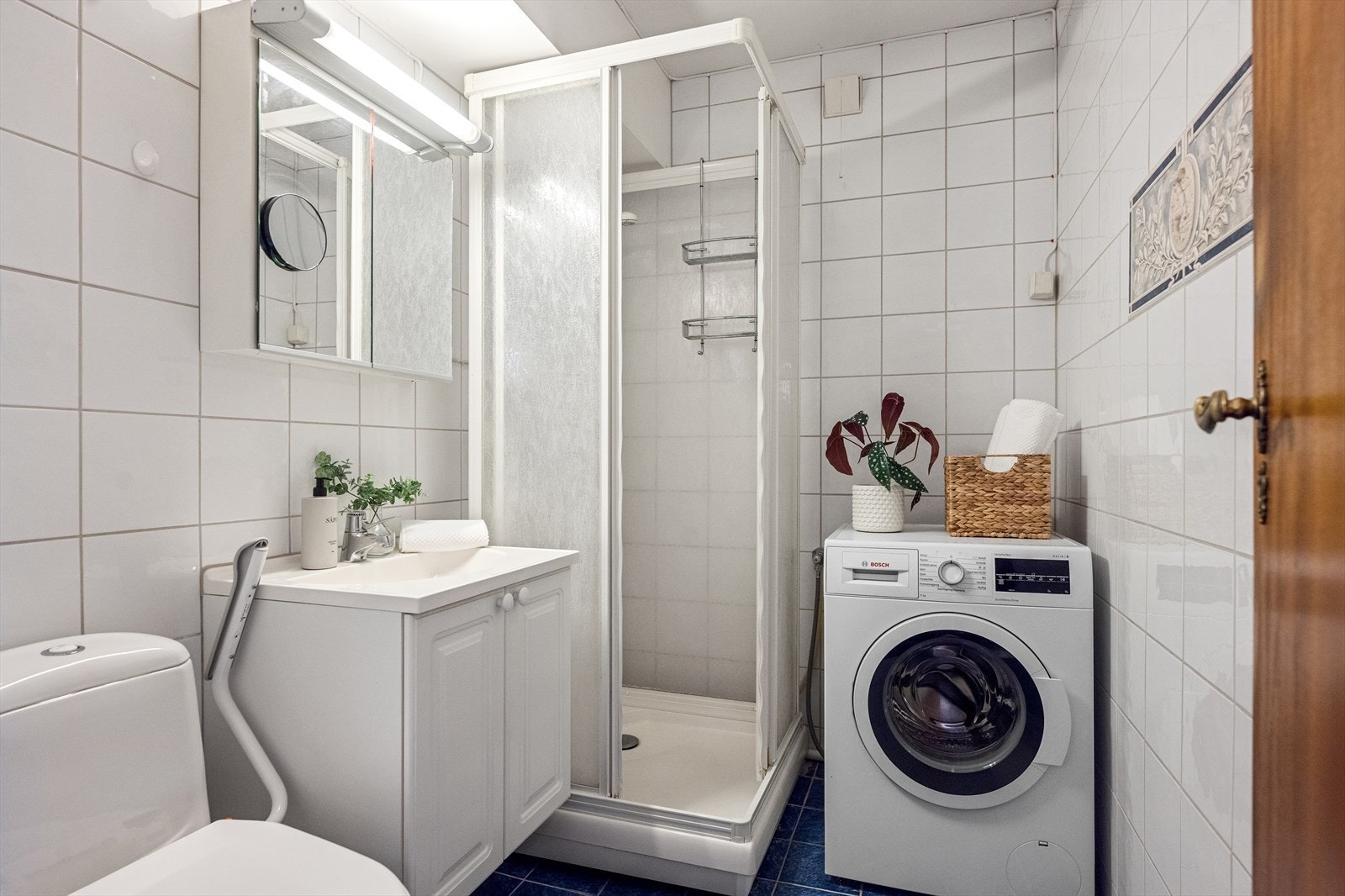 Badet er flisalgt på gulv og vegger samt innredet med dusjkabinett, toalett, servant i skapinnredning, speil med oppbevaring og opplegg for vaskemaskin. Galleribilde