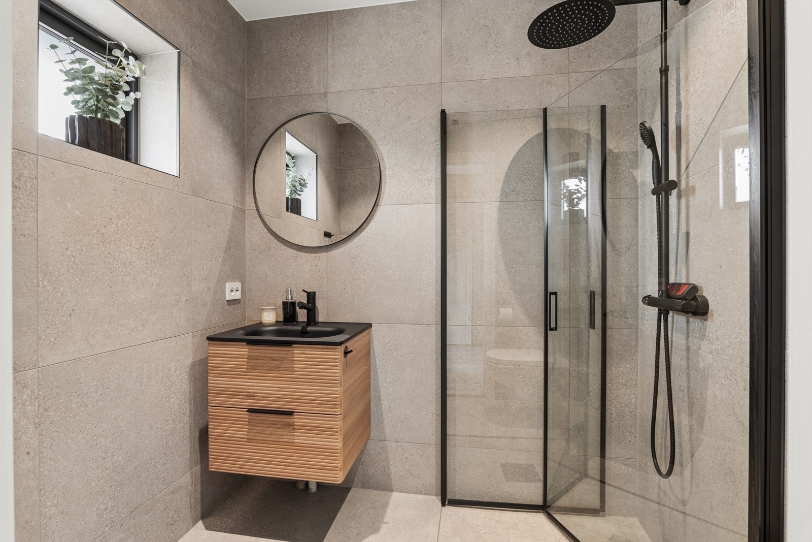 Lekkert bad med fliser på vegger og gulv med gulvvarme. Badet er innredet med servant med skuffeseksjon, dusjhjørne og veggmontert toalett. Galleribilde