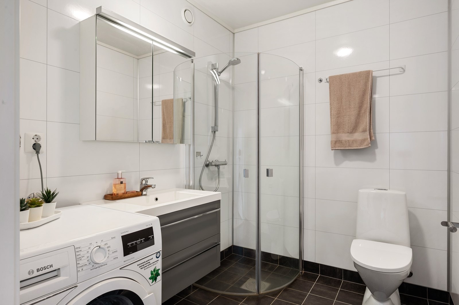 Badet har innhold av servant med benkeskap og speilfront, vegghengt toalett, dusjhjørne og opplegg for vaskemaskin. Galleribilde