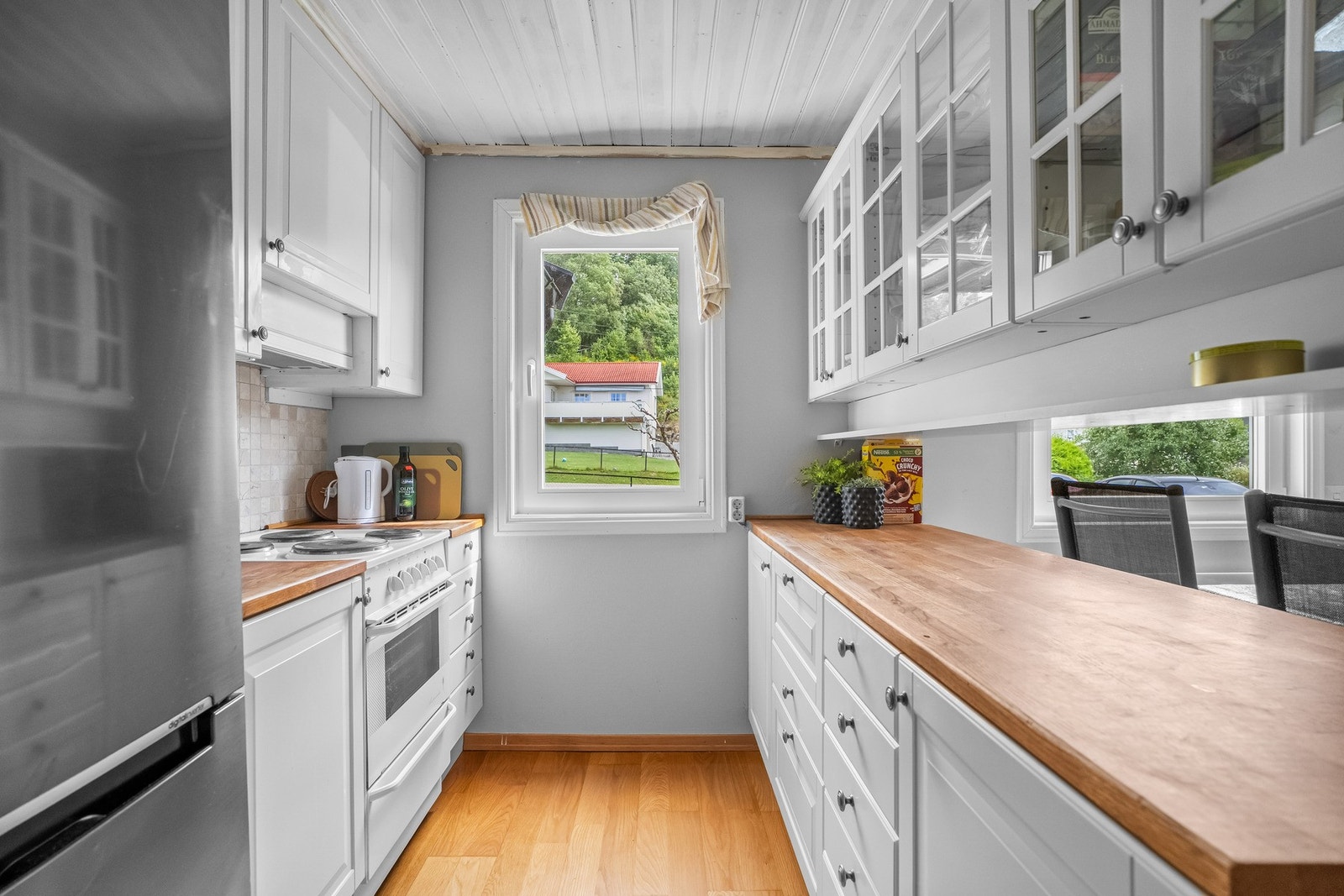 Kjøkkeninnredning med profilerte fronter, fliser på vegg over benkeskap, belysning under overskap og enkelte overskap med glassfronter. Heltre benkeplate, benkebeslag i rustfritt stål med utslagskum og kum. Galleribilde
