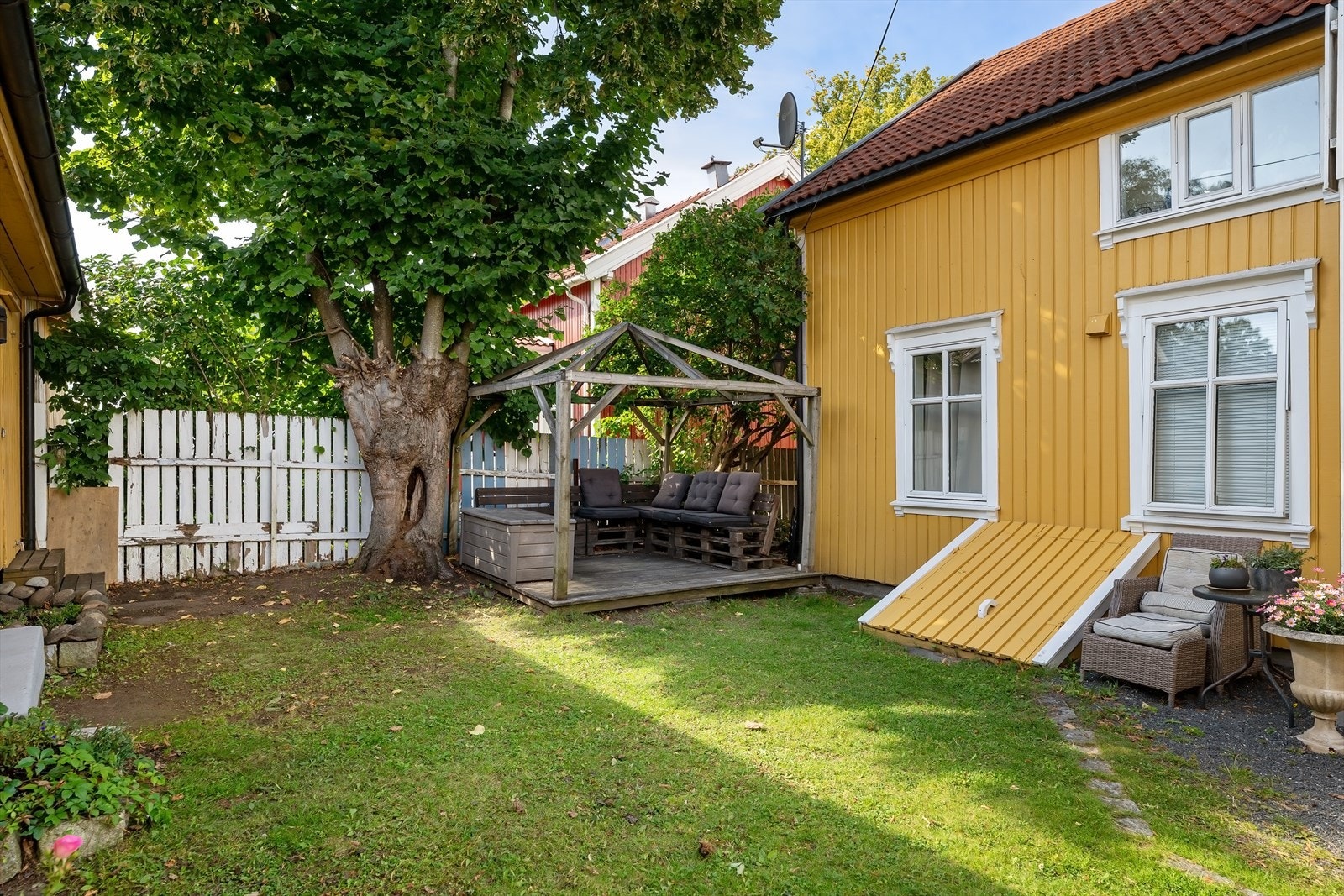 En trivelig bakgård med plen, et karakterfullt gammelt tre, bed og platting gir mulighet for å nyte en kaffekopp ute i solen. Galleribilde