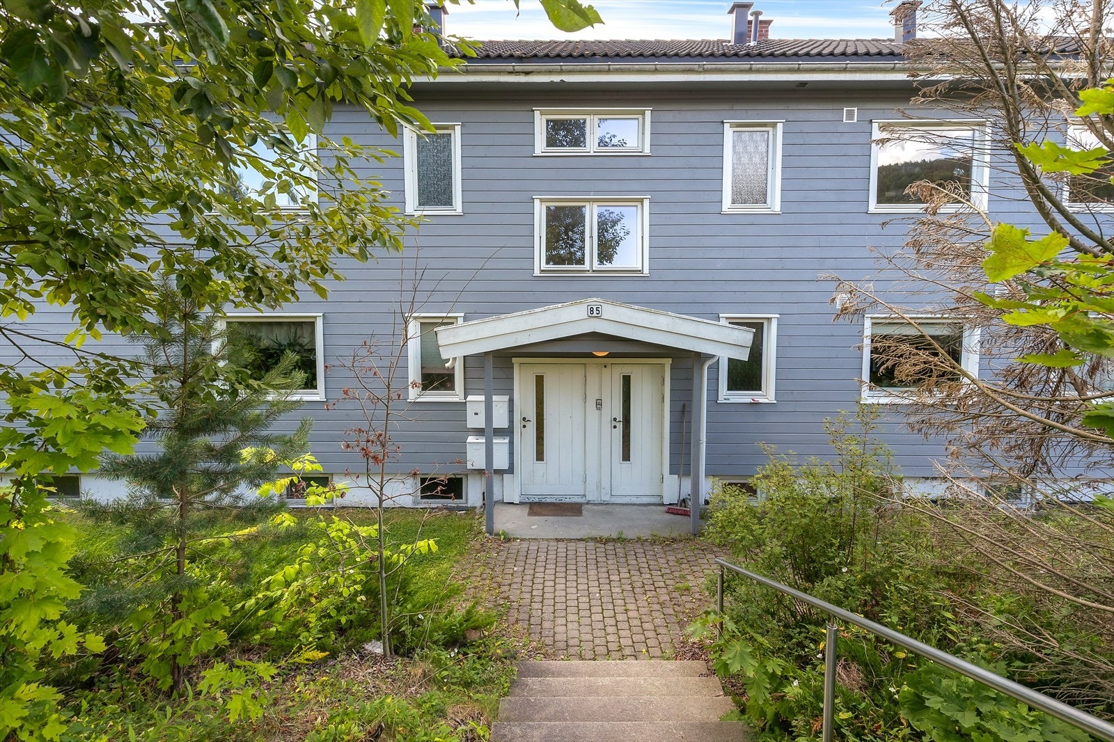 Det er trapp i terrenget og steinlagt plass foran inngangspartiet. Galleribilde