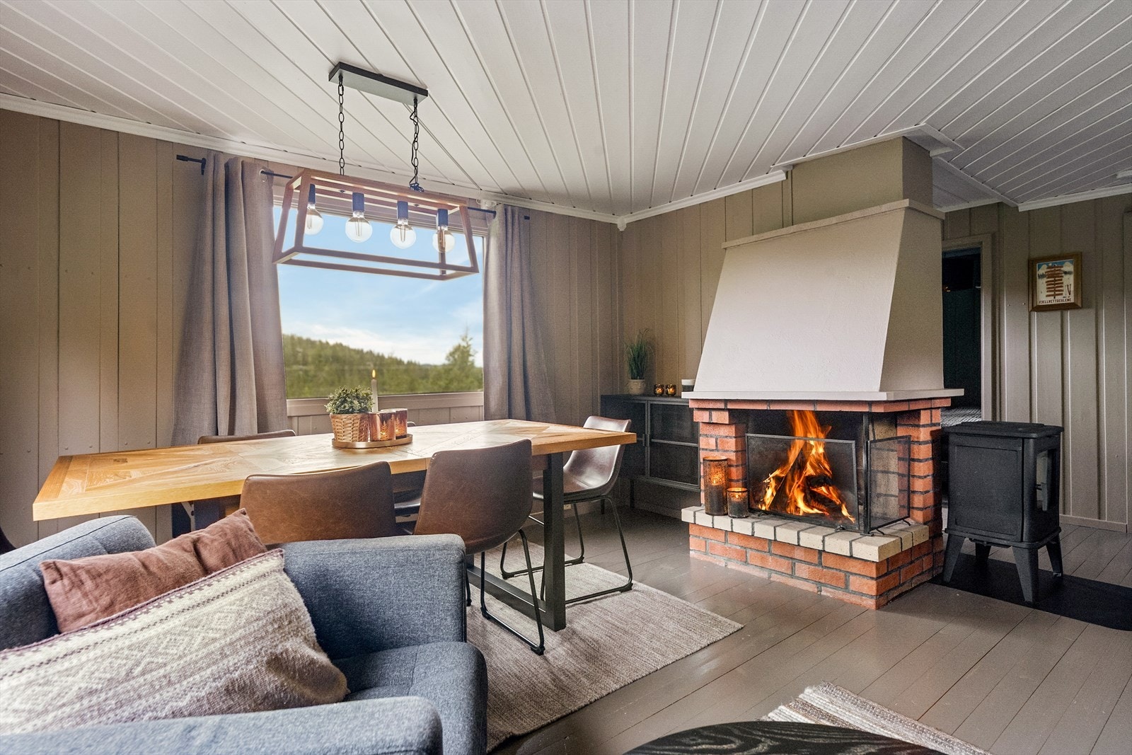 Stuens midtpunkt er en mursteinspipe med både vedovn og åpen grue for varme og hygge. Galleribilde