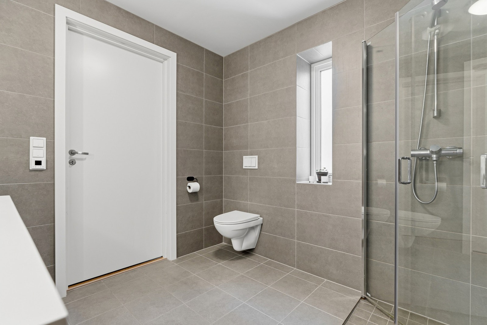 Badet har en helhetlig utførelse med flislagte overflater og god plass rundt dusjsonen. Galleribilde