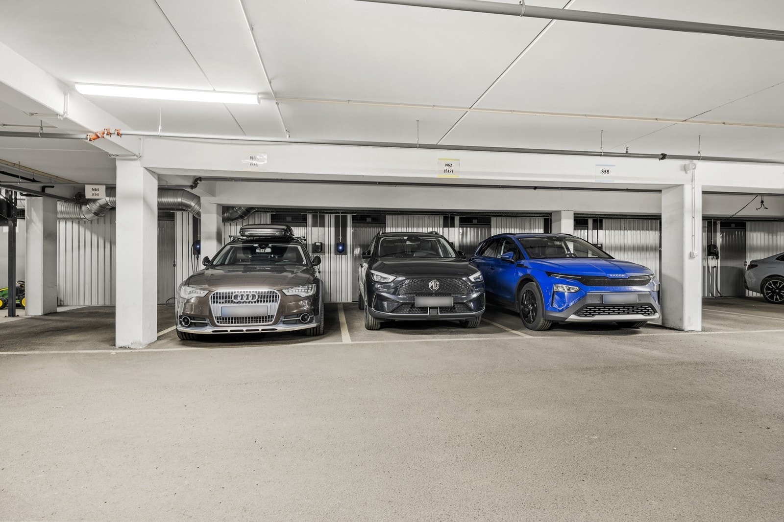 To tilhørende parkeringsplasser i felles anlegg. Den ene plassen (S32) har elbillader og den andre plassen (N63) har bod i bakkant. Galleribilde