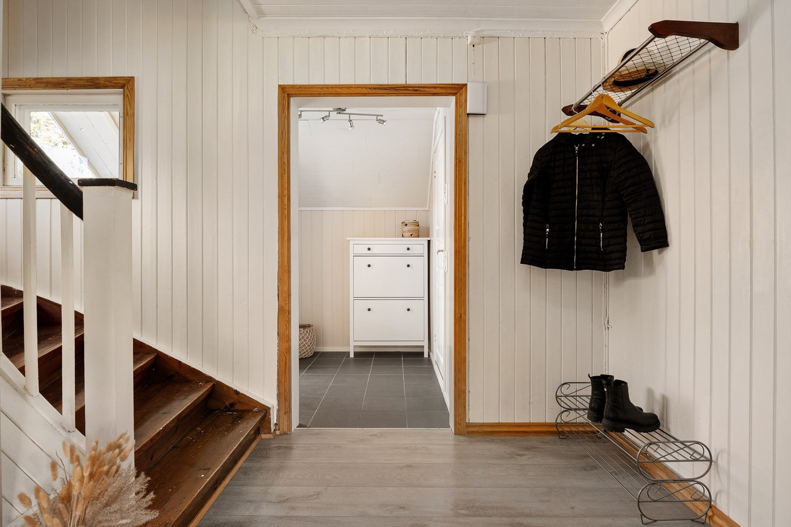 Herfra er det videre adkomst til boligens øvrige rom i 1. etasje og trappeløp som binder etasjene sammen. Gangen har parkett på gulv og malte paneloverflater. Galleribilde