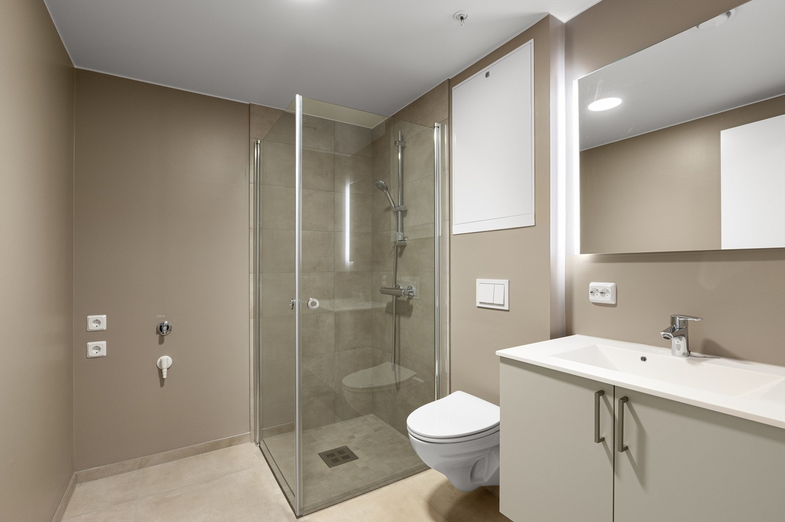 Badet er moderne og stilrent, med 60 × 60 cm gulvfliser, servant med baderomsinnredning, vegghengt toalett og dusjhjørne. Galleribilde