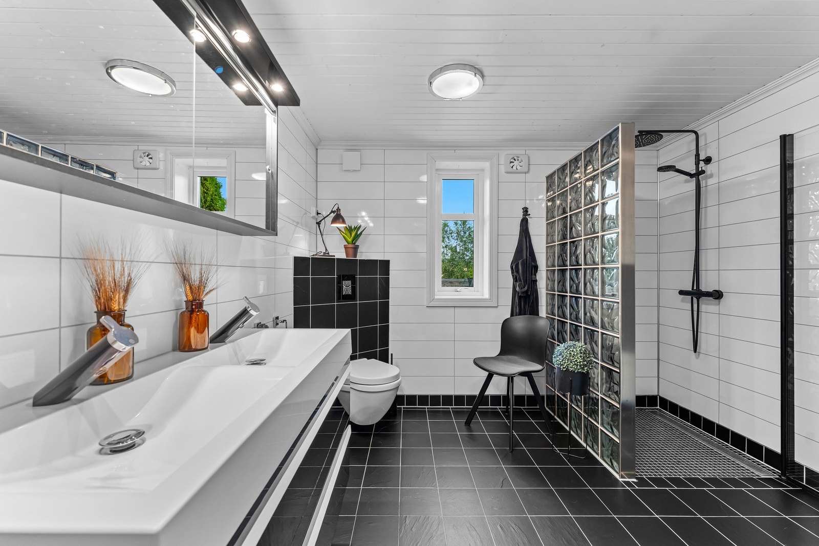 Det romslige badet har et stilrent sort-hvitt uttrykk og er innredet med dusjsone, toalett og dobbel servantinnredning. Galleribilde