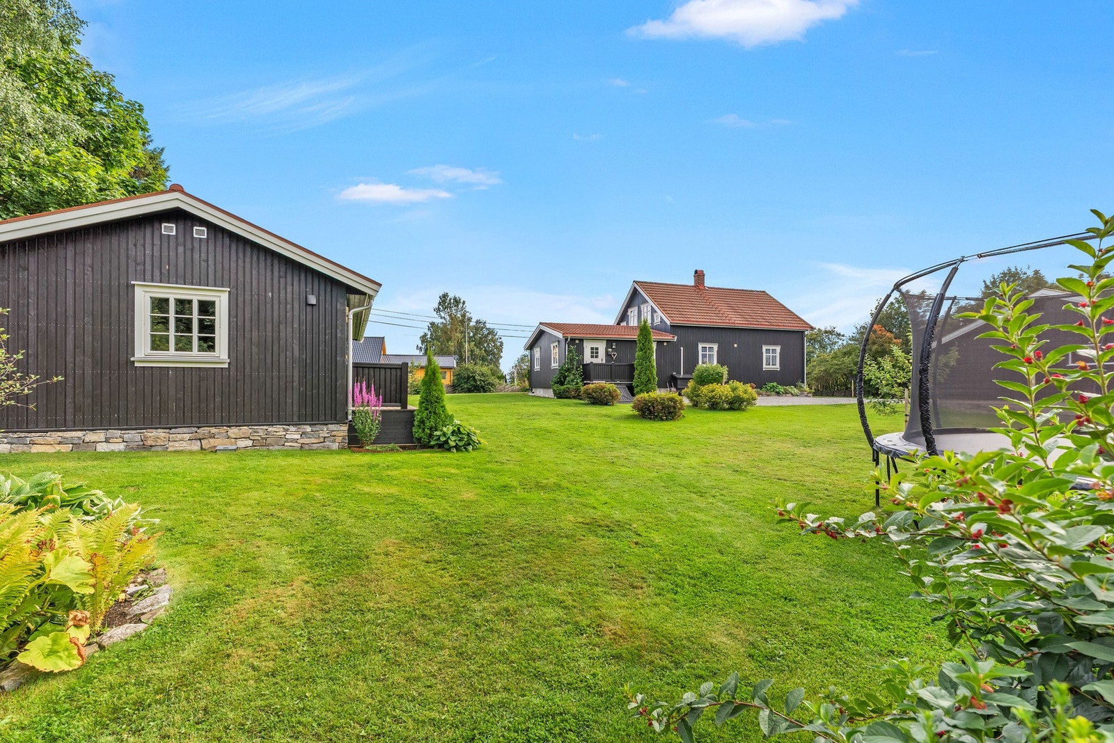 En stor og frodig hage gir rikelig med boltreplass, samtidig som etablert beplantning skaper en lun og hyggelig ramme rundt eiendommen. Galleribilde