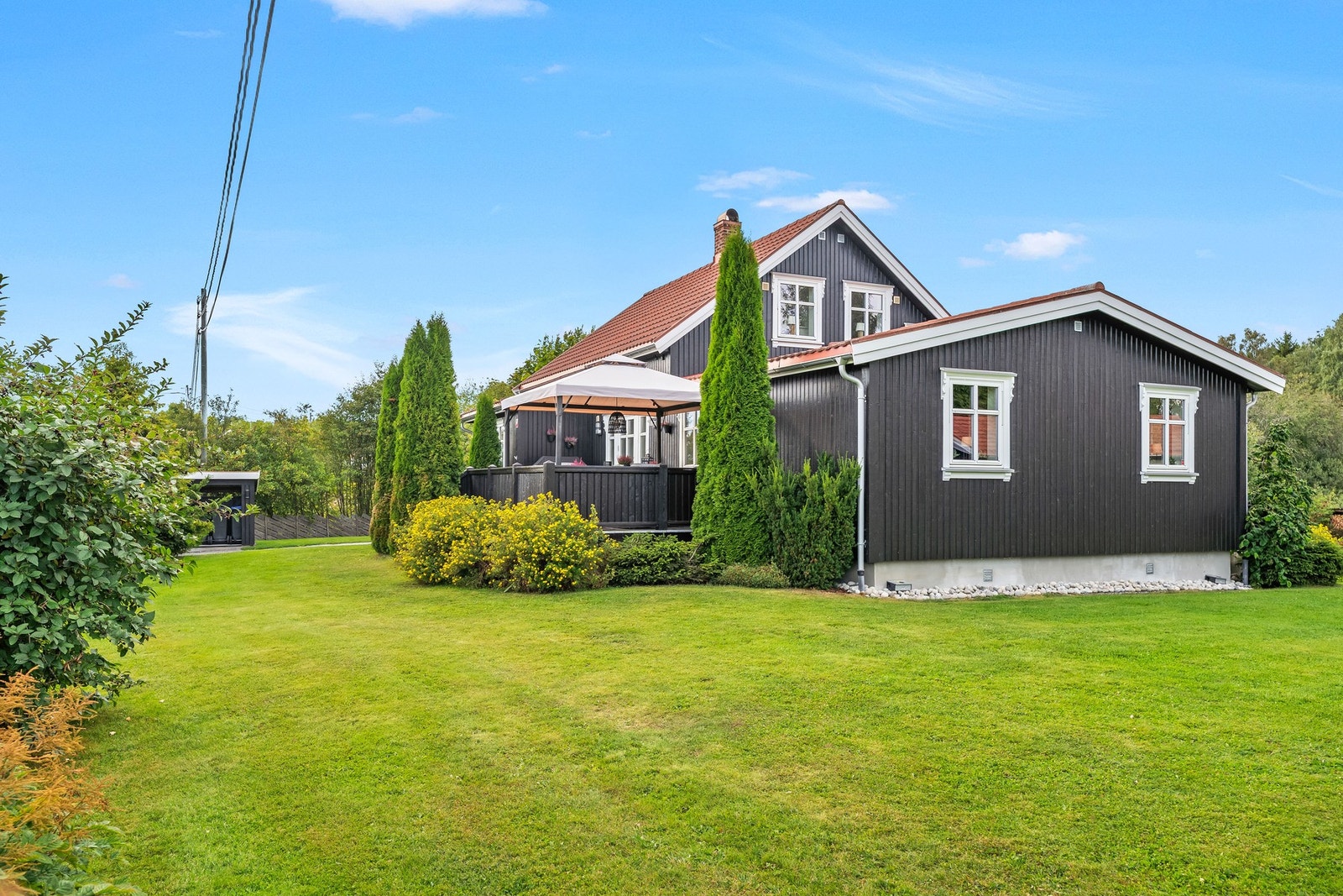 Den mørke trefasaden, de klassiske vinduene og den frodige hagen gir boligen et sjarmerende uttrykk som passer perfekt inn i de landlige omgivelsene. Galleribilde