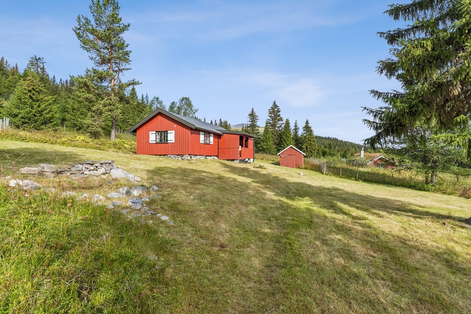 Tomten er skrånende og opparbeidet med plen og gjerde. Galleribilde