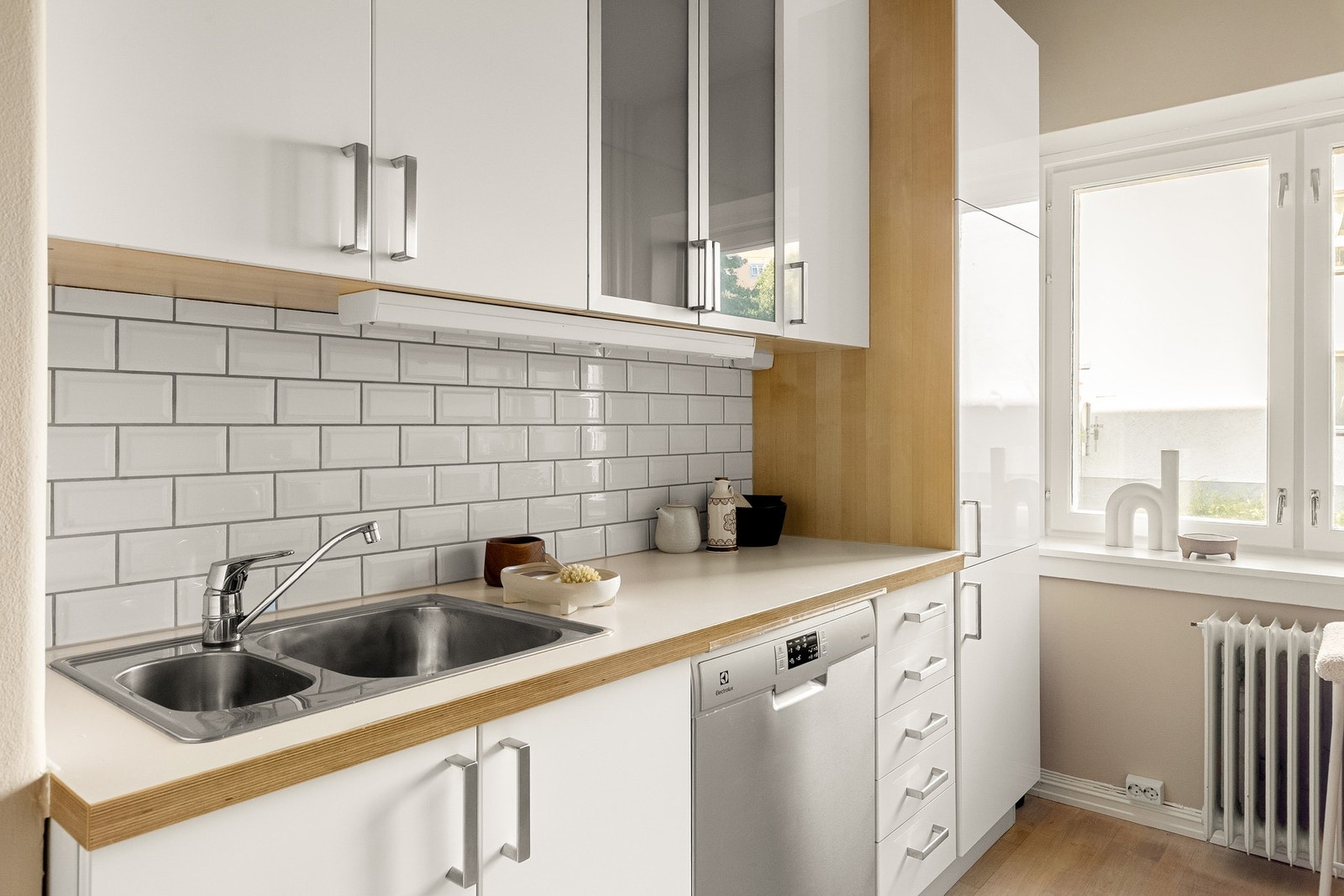 Kjøkkeninnredningen er utstyrt med hvite glatte fronter, vitrinedører med frostet glass, benkeplate i laminat med nedfelt kum i rustfritt stål og belysning under overskap. Galleribilde