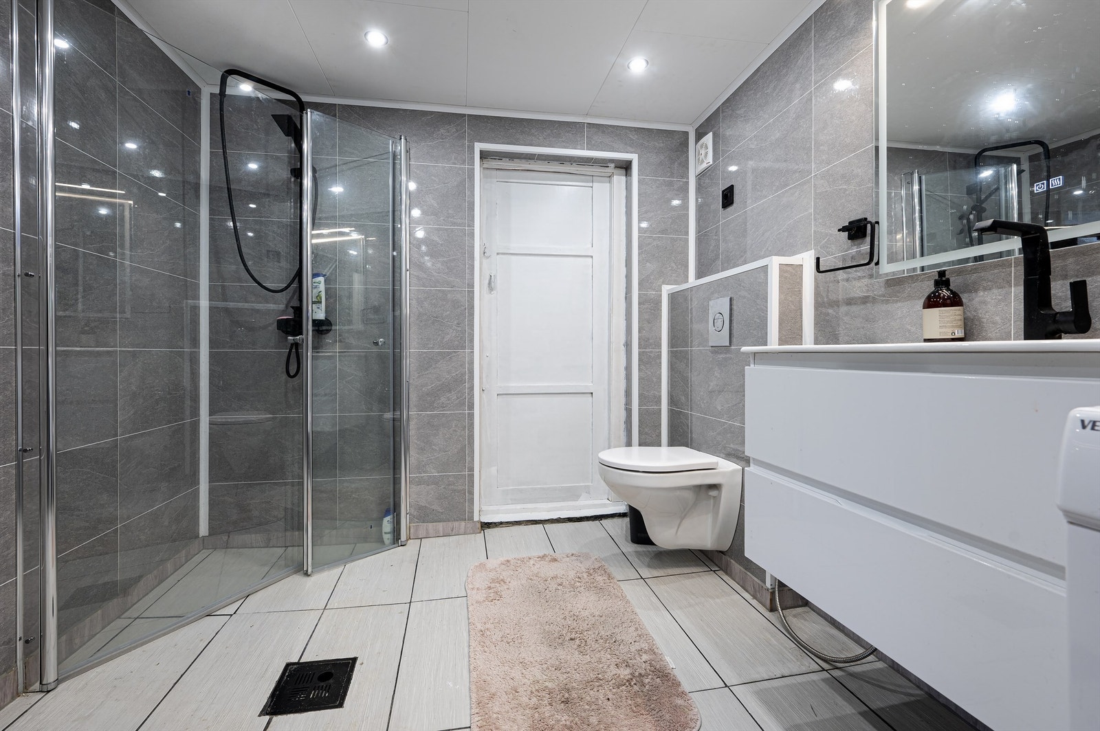 Badet har dusjhjørne, vegghengt toalett og baderomsplater på veggene. Galleribilde