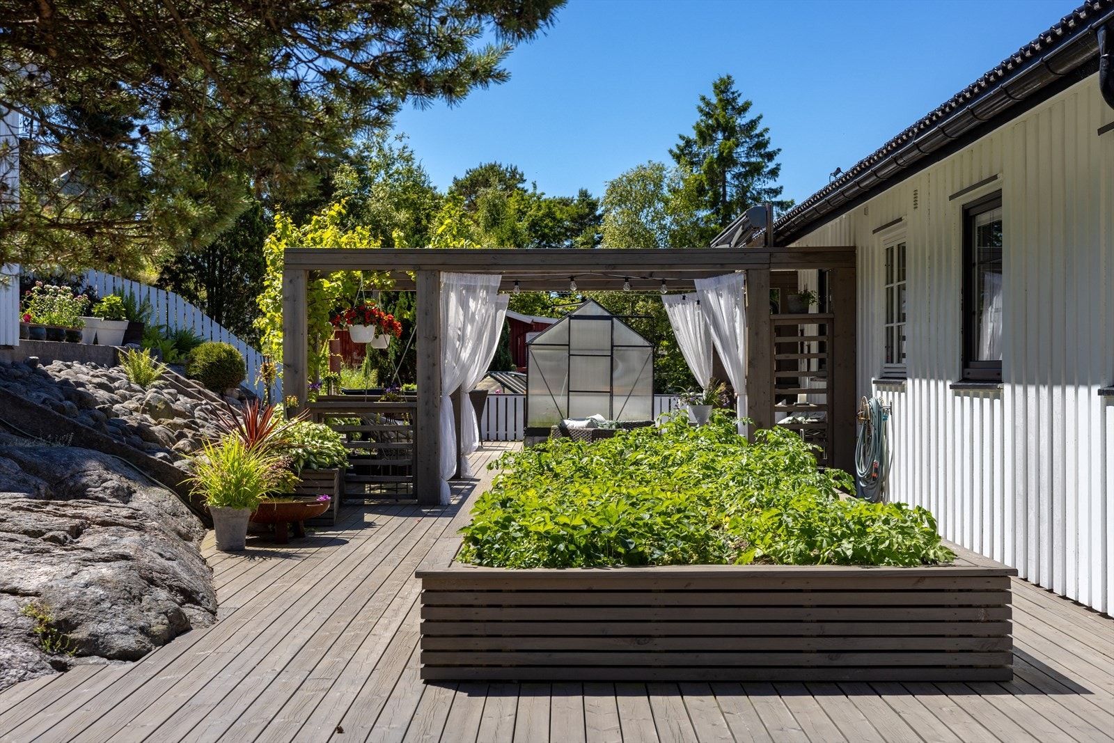 På husets bakside brer det seg en diger terrasse der du blant annet kan sitte under en bevokst pergola kledd med drueplanter. Det er også et grønnsaksbed i behagelig høyde hvor du kan så det du måtte ønske å høste i løpet av sommer og høst-sesongen. Galleribilde