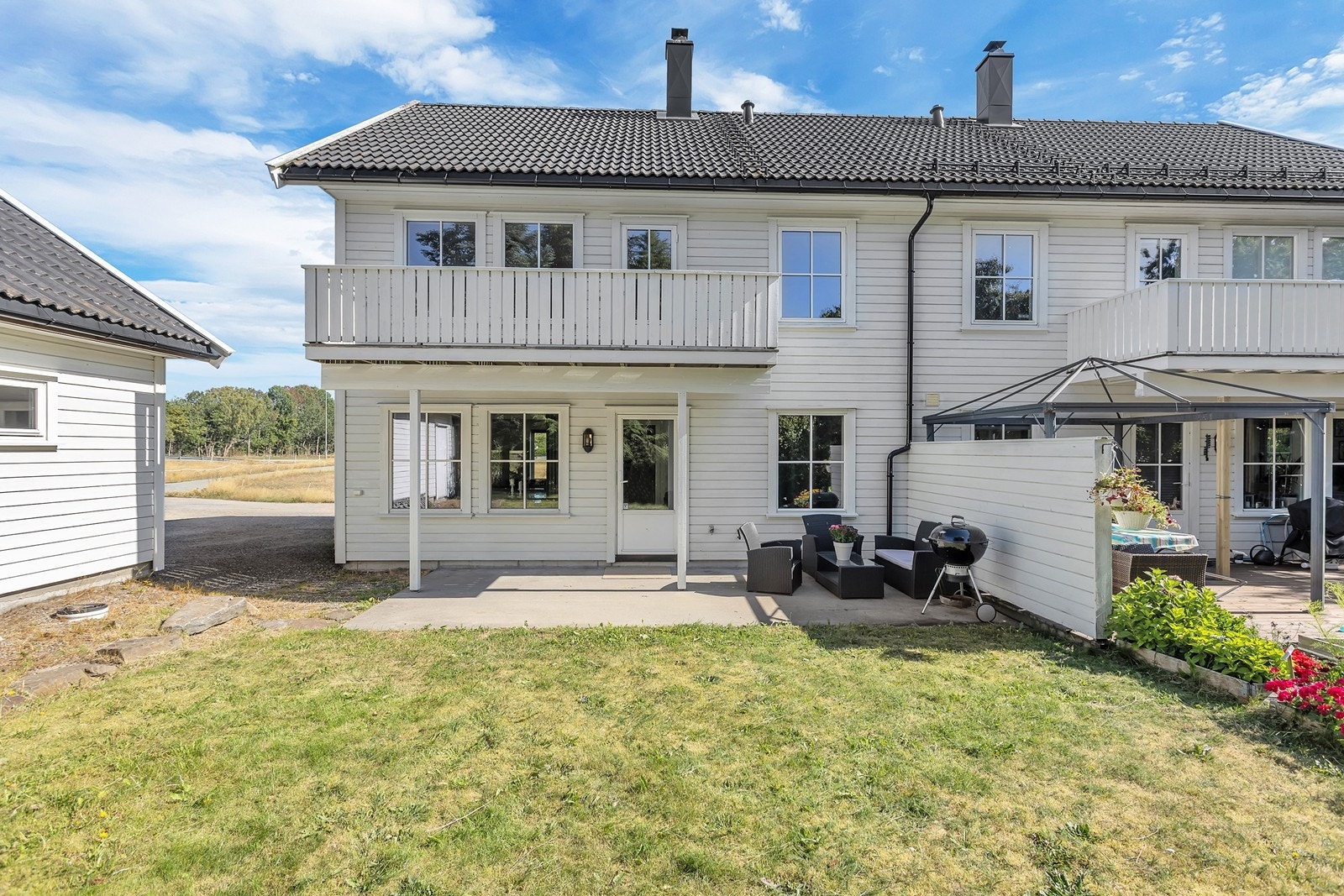 Baksiden av boligen byr på solrik terrasse og hage i grønne omgivelser, med balkong i 2. etasje. Galleribilde