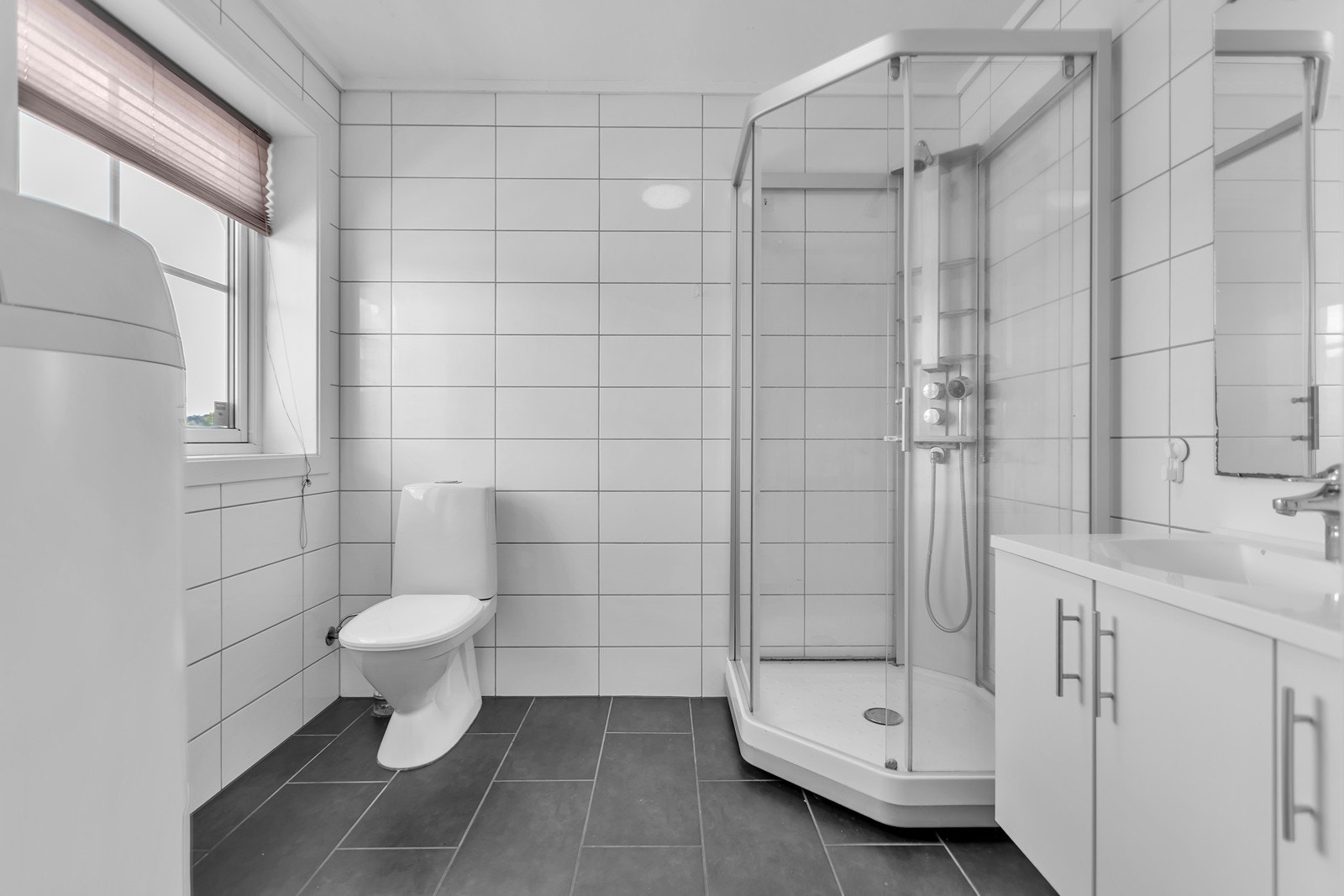 Badet fremstår lyst og tidsriktig med flislagte overflater, romslig dusjhjørne og et innbydende servantskap. Galleribilde