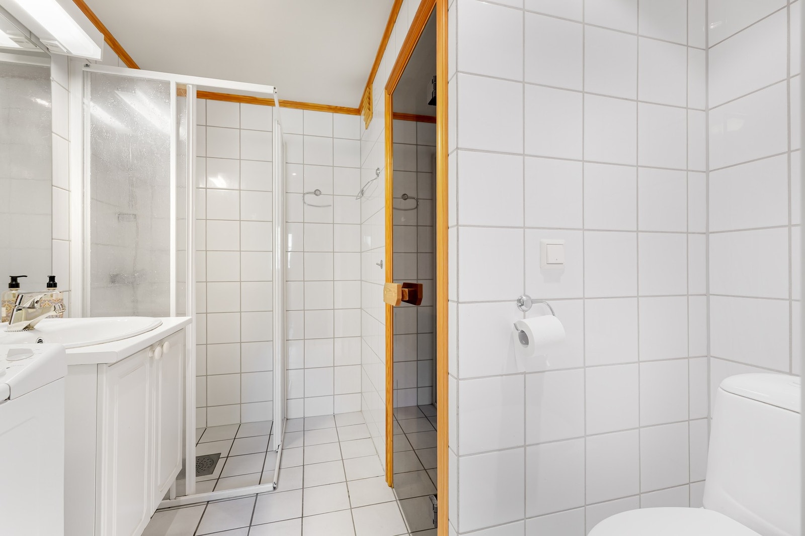 Leiligheten har to bad, ett i hver etasje. Badene har lik utførelse med hvite fliser på gulv og vegger, lys baderomsinnredning, toalett og dusjnisje med skyvedører. Galleribilde