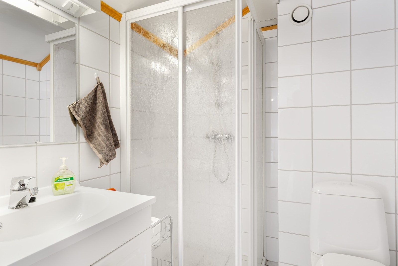 Badet i loftsetasjen har hvite fliser på gulv og vegger, lys baderomsinnredning, toalett og dusjnisje med skyvedører. Galleribilde